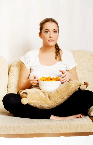 Молода жінка дивиться телевізор і їсть фішки — стокове фото