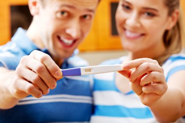 Young happy couple with pregnancy test standing in kitchen clipart