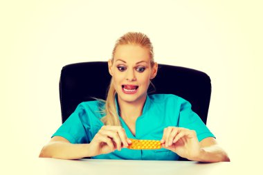 Şok ve korkmuş kadın hemşire ya da doktor arkasında oturan Resepsiyon ve paket hap holding