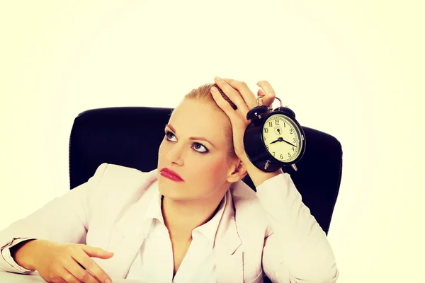 Уставшая деловая женщина сидит за столом и держит будильник — стоковое фото