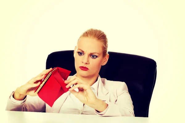 Mujer de negocios preocupada sentada detrás del escritorio con la cartera vacía —  Fotos de Stock