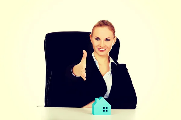 Zakelijke vrouw met een open hand klaar voor handdruk en blauw papieren huis op het bureau — Stockfoto