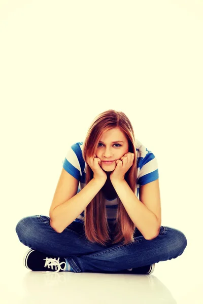 Mulher adolescente sorridente sentada em um chão com as pernas cruzadas — Fotografia de Stock