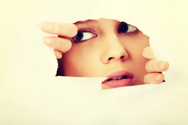 Teenage woman peeping through hole on paper — Stock Photo, Image