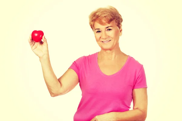 Old smiling woman holding red toy heart — Stock Photo, Image