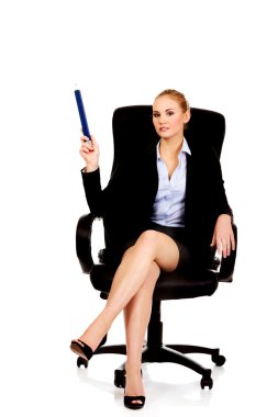 Genç iş kadını koltuğunda oturuyor ve büyük bir kalemle işaret ediyor.