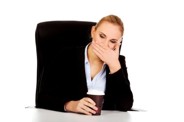 Tired business woman with coffee in paper cup behind the desk clipart