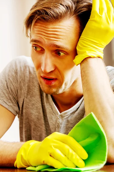 Tired man sitting behind the desk with cloth and gloves — Stock Photo, Image