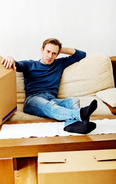 Uomo stanco seduto sul divano con scatole di cartone intorno — Foto Stock