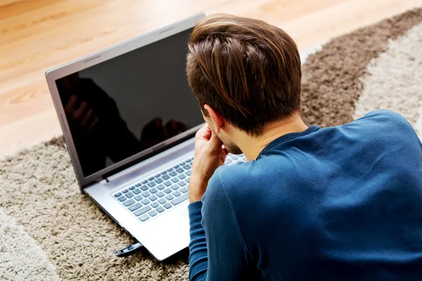 Młody człowiek leży na podłodze i używa laptopa — Zdjęcie stockowe