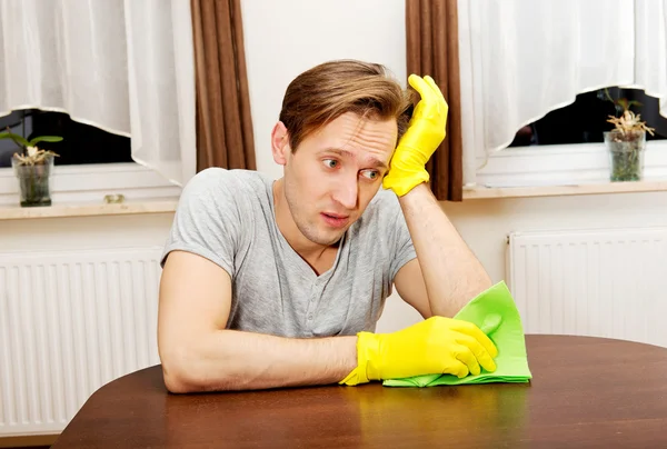 Homem cansado sentado atrás da mesa com pano e luvas — Fotografia de Stock