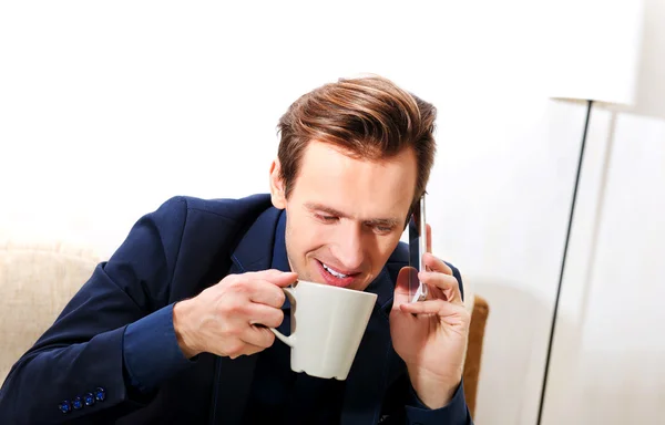 Boldog fiatal üzletember, beszél a telefonon keresztül, és az ivás, kávé vagy tea — Stock Fotó
