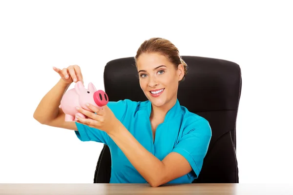 Médica jovem ou enfermeira segurando piggybank — Fotografia de Stock