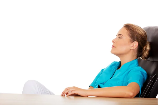 Tired young female doctoror nurse sitting behind the desk — Stock Photo, Image