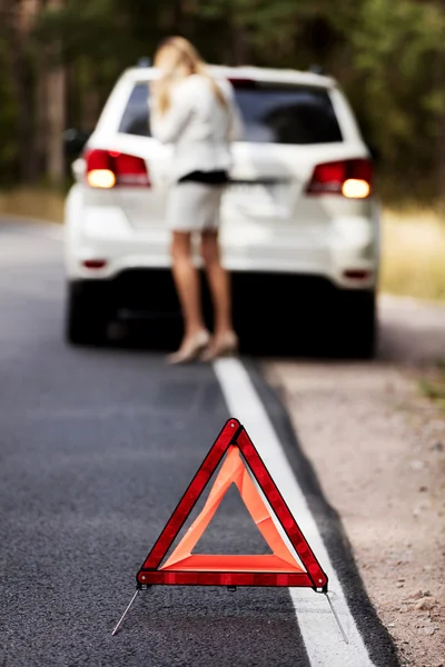 Red warning triangle and broken car in the middle of forrest — Stock Photo, Image