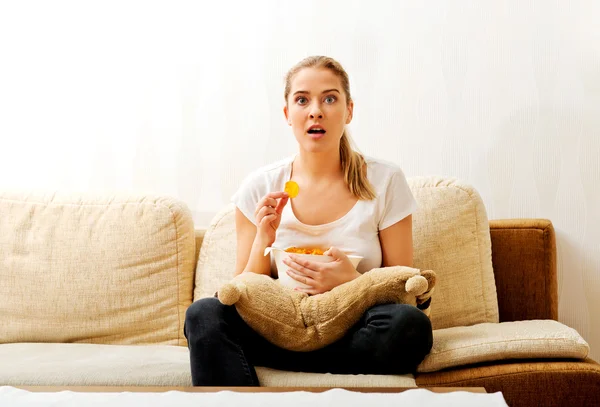 Giovane donna guardando la TV e mangiare patatine fritte — Foto Stock