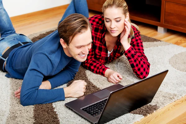 Casal feliz deitado no chão com laptop — Fotografia de Stock