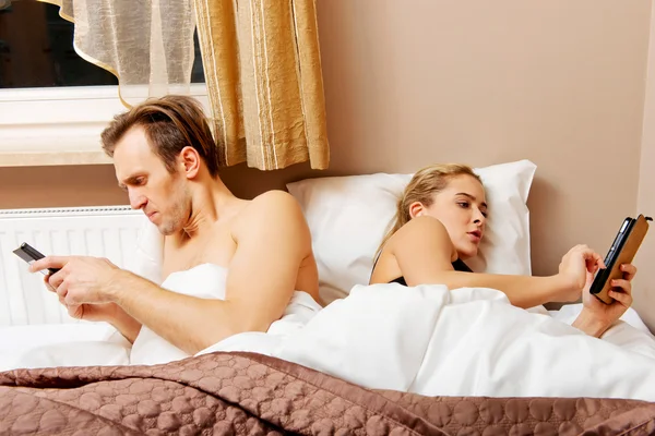 Genç mutlu çift cep telefonlarıyla yatakta.