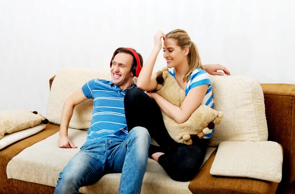 Пара расслабляется на диване, мужчина слушает музыку женщина обнимает его — стоковое фото