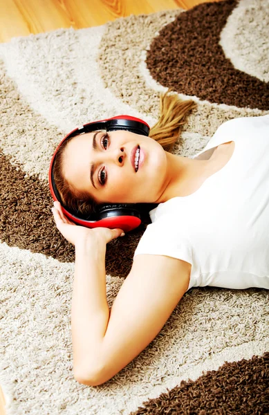 Молодая женщина лежит на ковре и слушает музыку в наушниках — стоковое фото