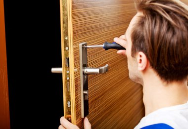 Genç adam tornavidayla kapıyı tamir ediyor.