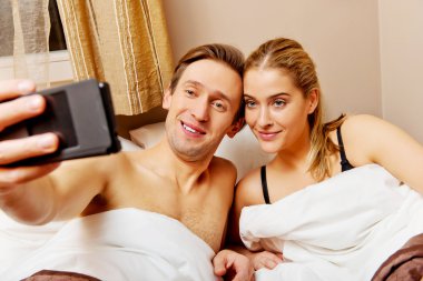 Genç çift yatakta yatarken selfie çekiyor.