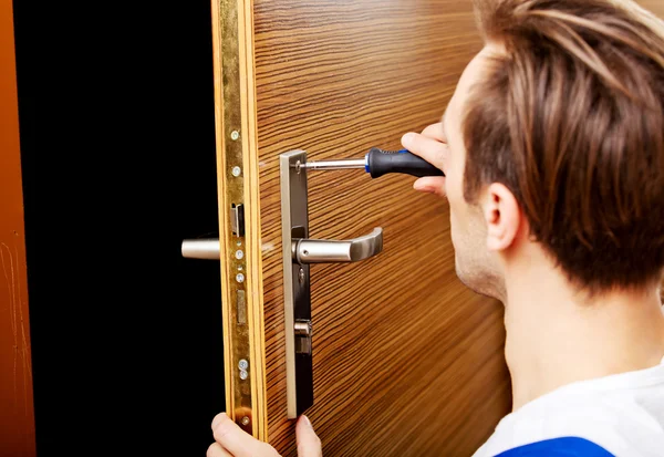 Genç adam tornavidayla kapıyı tamir ediyor.