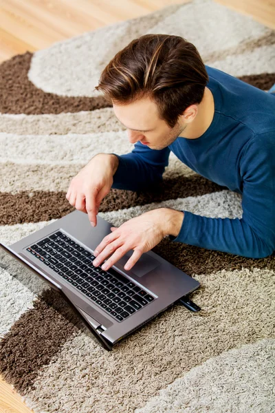 Ung man som ligger på golvet och använder laptop — Stockfoto