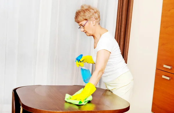 Ältere Frau in gelben Handschuhen putzt Tisch — Stockfoto