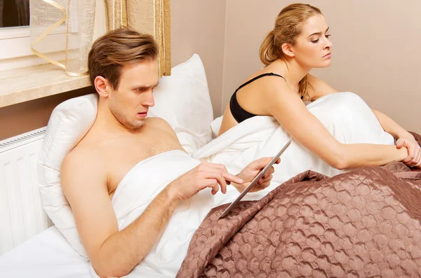 Yatakta bir çift, tabletli kadın kullanan bir adam sıkılmış oturuyor. — Stok fotoğraf