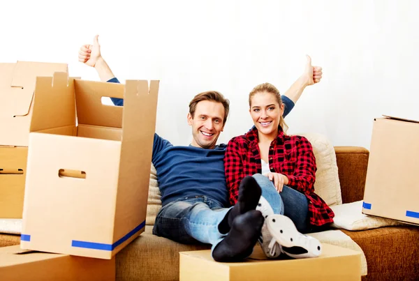 Happy tired couple sitting on couch in new home with cordboard boxes around — Stock Photo, Image