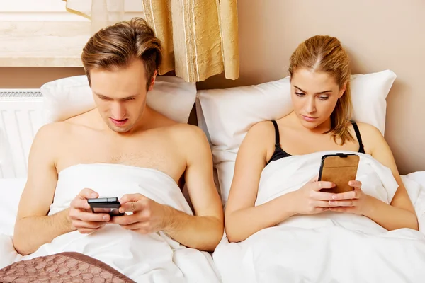 Jong gelukkig paar in een bed met mobiele telefoons — Stockfoto