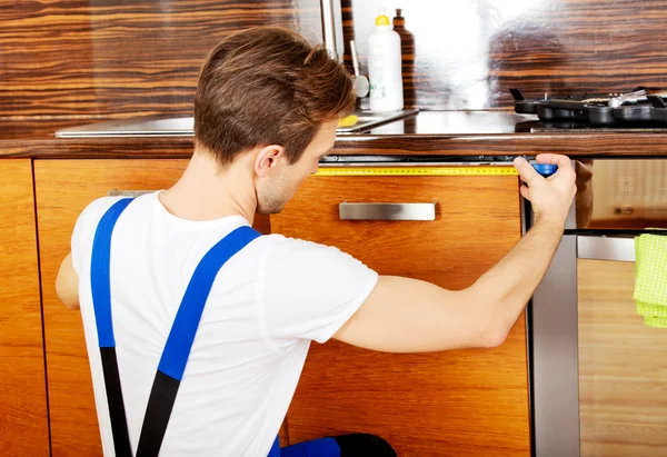测量厨房橱柜的年轻修理工 — 图库照片