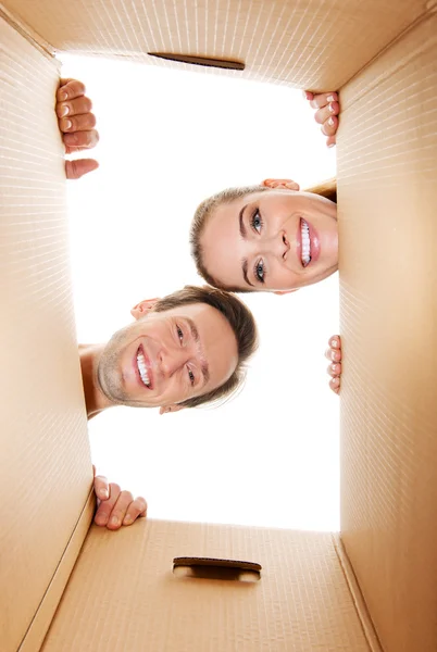 Happy young couple opening a carton box and looking inside — Stock Photo, Image