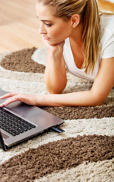Focused young woman using laptop while lying on floor — Stock Photo, Image