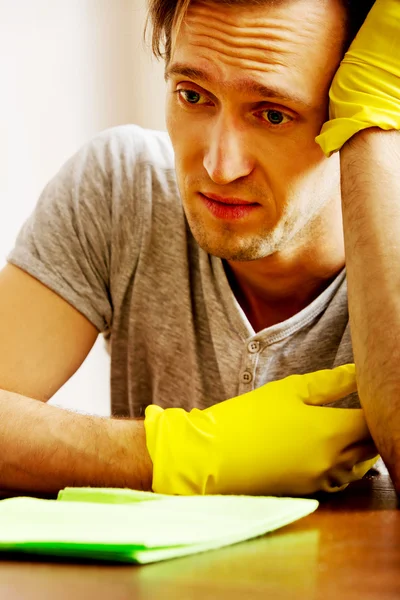 Tired man sitting behind the desk with cloth and gloves — Stock Photo, Image