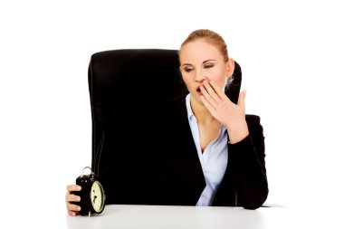 Tired business woman behind the desk with alarm clock clipart
