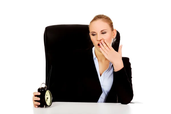 Müde Geschäftsfrau hinter dem Schreibtisch mit Wecker — Stockfoto