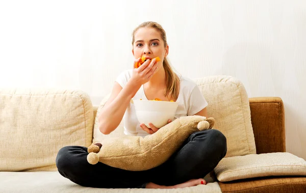 Mujer joven viendo la televisión y comiendo patatas fritas —  Fotos de Stock