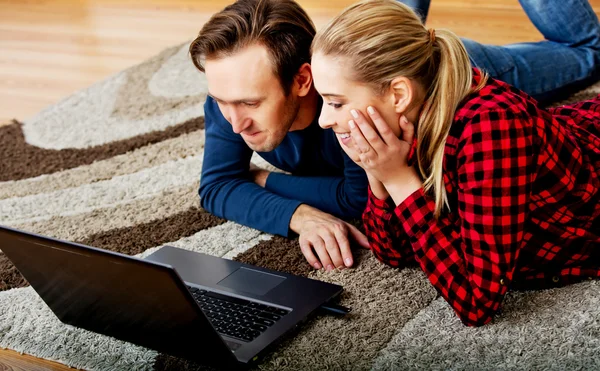 Glada par ligger på golvet med laptop — Stockfoto