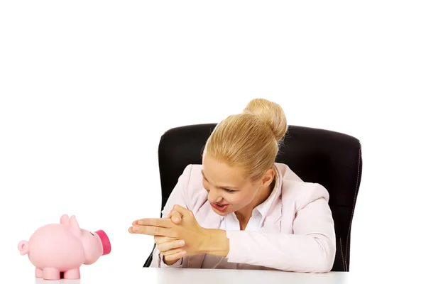 Funny business woman shooting to her piggybank with gun gesture — Zdjęcie stockowe