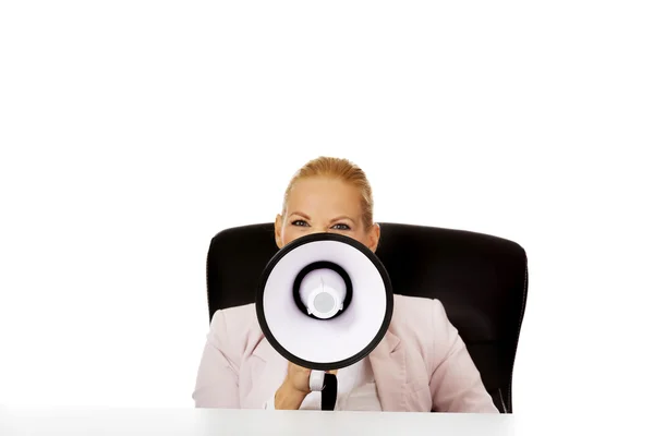 Zakelijke vrouw zit achter het bureau en schreeuwen door een megafoon — Stockfoto