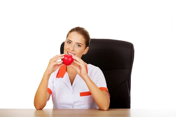 Vrouwelijke arts zitten achter de balie en het bedrijf hart speelgoed — Stockfoto