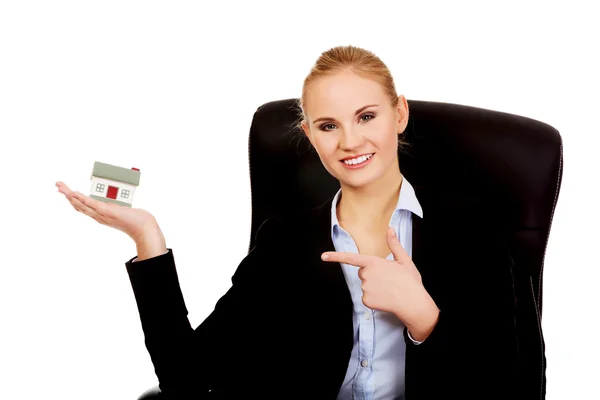 Χαμογελαστή γυναίκα των επιχειρήσεων κάθεται σε μια καρέκλα και κρατώντας πατημένο το σπίτι μοντέλο — Φωτογραφία Αρχείου