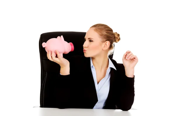 Glückliche Geschäftsfrau mit Sparschwein hinter dem Schreibtisch — Stockfoto