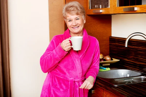 Elderly smile woman drinking coffee or tea in her kitchen — Stock Photo, Image