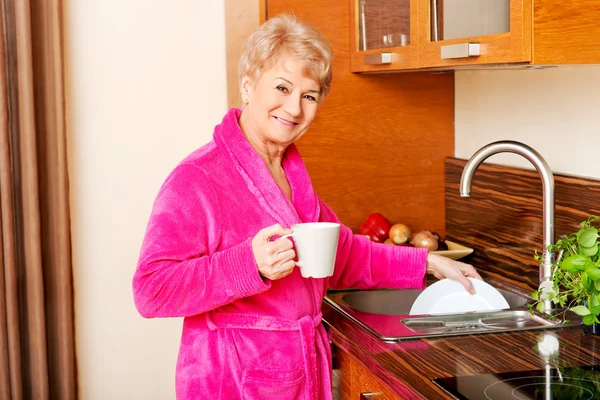 Senior kvinna dricker kaffe i kök och tvättplatta — Stockfoto
