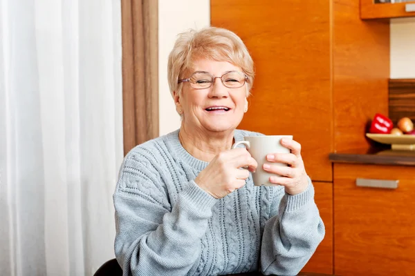 Mujer mayor sentada en el escritorio y tomando café o té — Foto de Stock