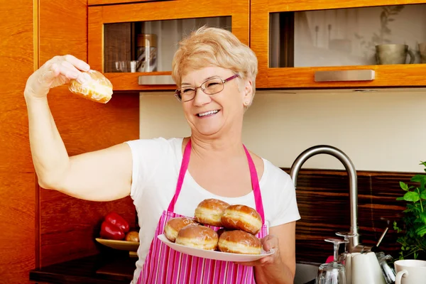 Kıdemli kadın elinde donut tabağı tutuyor. — Stok fotoğraf