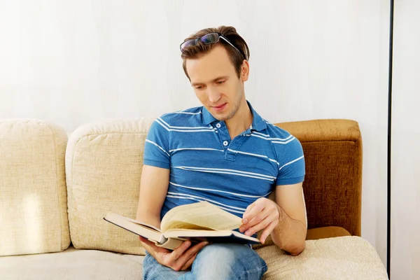 Man sitting on couch and reading book — Stock Photo, Image